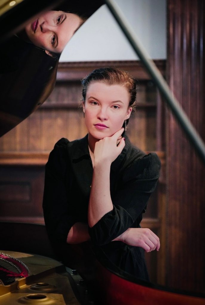 Sage Fogle sits at a piano and is reflected in the piano